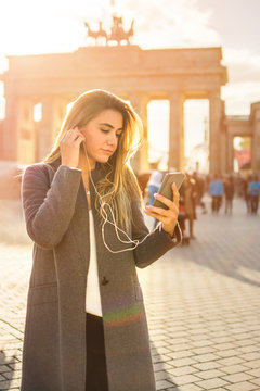 Beautiful young woman listening to music on mobile phone while standing near Brandenburg gate in Berlin.