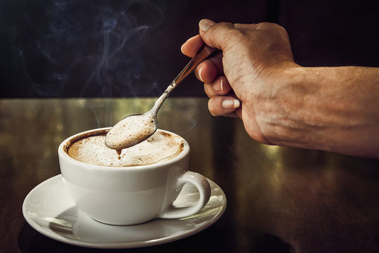 A Woman Holding Coffee Spoon To Stir Hot Coffee On Wooden Table