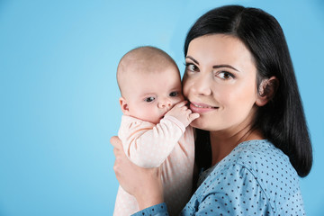 Young mother and cute baby on color background