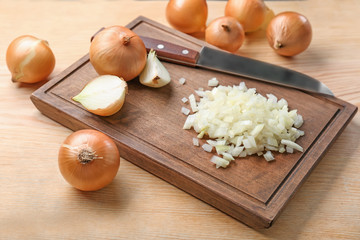 Board with sliced yellow onion and knife on wooden background
