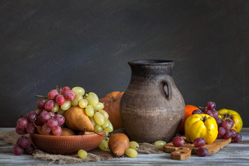 Still life in a rustic style: a set of clay dishes, grapes and pears on a wooden table. Natural...