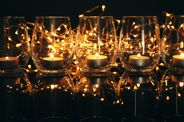 Glasses with burning candles on dark background