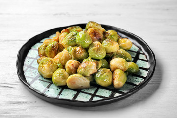 Plate with roasted Brussels sprouts on wooden table, closeup