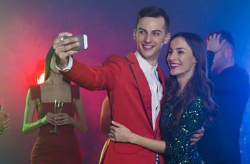 Photo from the party. Friends rest and dance in the club on holiday. The guy with the girl do selfie on the phone