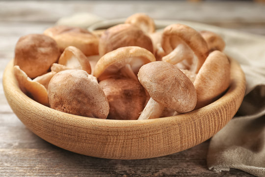 Bowl with raw shiitake mushrooms on wooden table, closeup