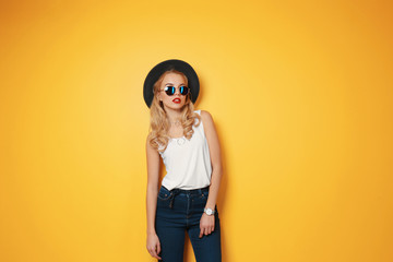 Attractive hipster girl with hat and sunglasses on color background