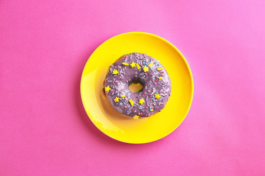 Plate with tasty glazed donut on color background