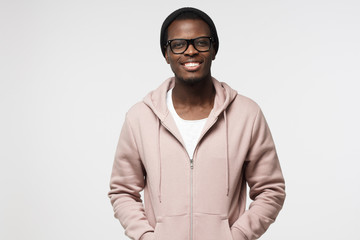 Portrait of smiling handsome african american guy in pink hoodie standing isolated on gray background