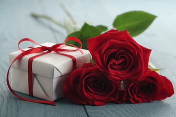 three red roses on blue wood table with gift box