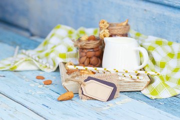 Almonds in the glass, jar with milk on the wooden tray and decorative tag