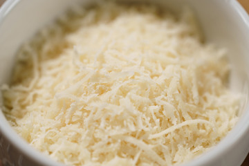closeup grated aged italian parmesan cheese in white bowl on table
