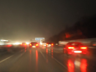 Starker Verkehr auf der Autobahn bei Nacht und Regen: Regennasse Frontscheibe, rote Rücklichter, Lichtreflexe