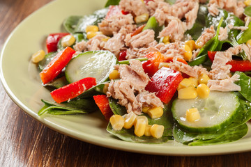 Fresh spinach salad with tuna, cucumber, corn, and red paprika on a plate