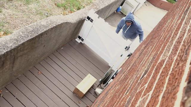 A clean high angle video feed showing a thief stealing a package from the side of a house in broad daylight when no one is home.  	