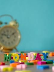 Colorful wooden word MONDAY on wooden table and vintage alarm clock and background is powder blue. English alphabet made of wooden letter color.