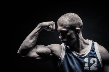 Obraz na płótnie Canvas portrait of a male bodybuilder, straining muscles in sports poses, on a black background is isolated. monochrome. The concept of a photo of competing sports, health, fitness