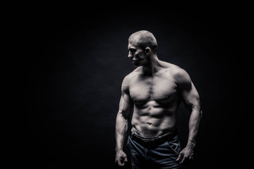 Obraz na płótnie Canvas portrait of a male bodybuilder, straining muscles in sports poses, on a black background is isolated. monochrome. The concept of a photo of competing sports, health, fitness