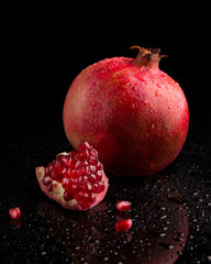 Ripe pomegranate fruits on a black background with water droplets