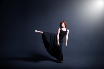 Dancer in a black dress is dancing in the dark studio