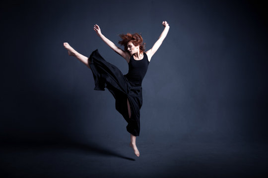 Dancer in a black dress is dancing in the dark studio