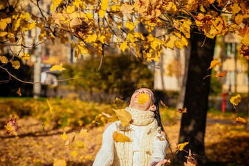 portrait of a beautiful young girl in fashionable business clothes walking along the autumn park, catching the falling leaves