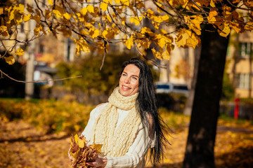 portrait of a beautiful young girl in fashionable business clothes walking along the autumn park, catching the falling leaves