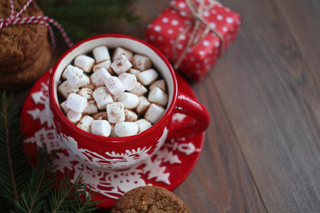 Red Christmas mug of coffee and marshmallows and gift box on the wooden table