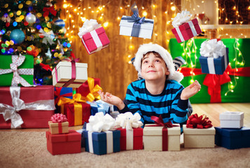 Fototapeta na wymiar Boy lying on the floor with presents near christmas tree. Child in red hat at home in winter