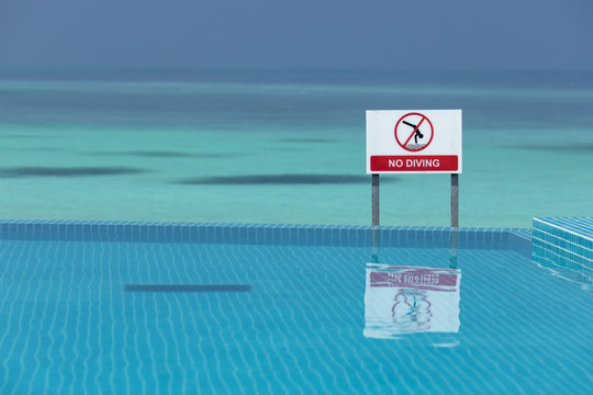 No diving sign at an infinity pool against the beautiful clear blue sea, with space for text