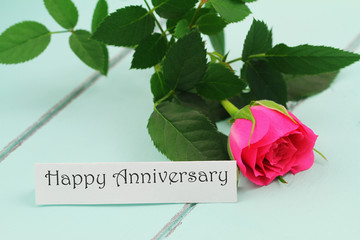 Happy Anniversary card with pink wild rose on wooden surface
