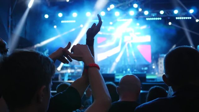 active youth claping with arms raised over head on event of live music in bright illuminated by floodlights at night in Slow motion