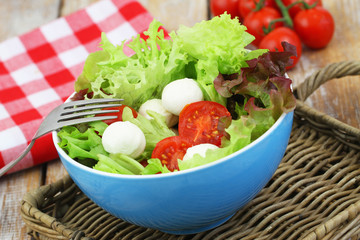 Salad with lettuce, mozzarella and cherry tomatoes in blue bowl, closeup
