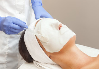 The cosmetologist for procedure of cleansing and moisturizing the skin, applying a Alginic mask to...