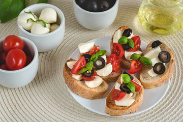 Bruschetta italian snack sandwiches with mozzarella, tomatoes and black olives decorated by basil leaves.