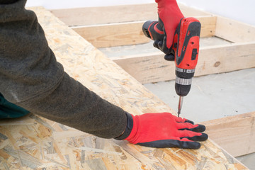 Man worker screws wooden oriented stands bords on insulated floor. New house constuction