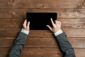 Top view of businesswoman sitting at wooden table and working with tablet