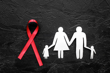 Red ribbon for HIV, AIDS, substance-abuse and anorexia awareness near paper silhouette of family on black background top view