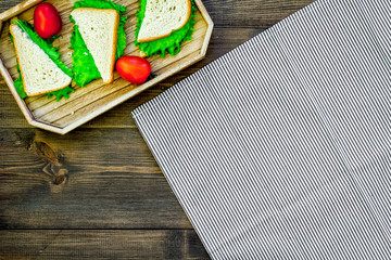 Sandwiches with lettuce and tomatoes for picnic on tablecloth on dark wooden background top view copyspace