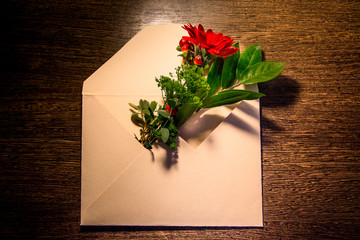 a bouquet of red gerbera flowers and a green branch lie in an envelope