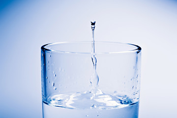 A glass of water. Water drop flying out from the glass.