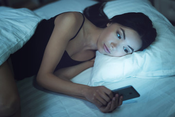 Girl is in a dark room in bed. She looks at the smartphone. Influence of social networks on youth.