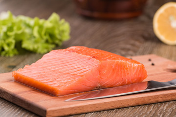 A piece of smoked salmon. On a wooden cutting board with a knife.