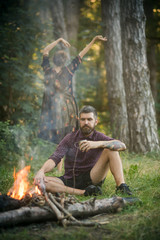 Man and woman relax at bonfire in forest