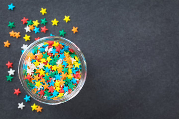 Colorful star shaped sugar sprinkles in glass jar, photographed overhead on slate (Selective Focus,...