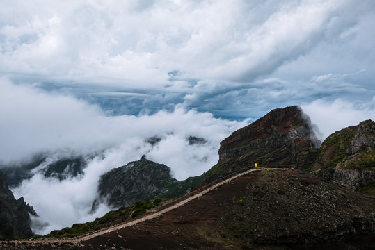 Adult male in yellow jacket gazing over a dramatic cloudscape and mountains on Madeira island, Portugal