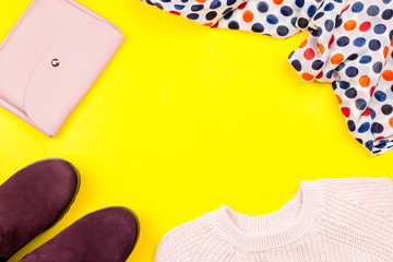 Stylish purple suede ankle boots, pink sweater, purse, spotted shawl on a bright background