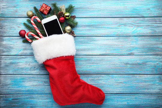 Red stocking with fir-tree branches and smartphone on wooden table