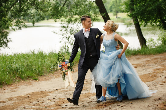 Creative wedding concept. Newlyweds couple walking in forest, bride in blue wedding dress and blue sport shoes