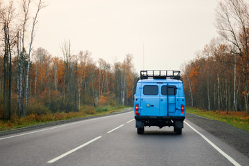 Fototapeta na wymiar A blue van driving on a road along the forest