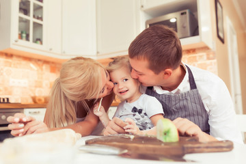 Obraz na płótnie Canvas Young parents and their beautiful and cute child girl cooking and eating breakfast ot lunch at kitchen table at home